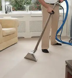 Professional carpet cleaner using a hot-water extraction wand and hose machine in a living room in Pueblo, CO.