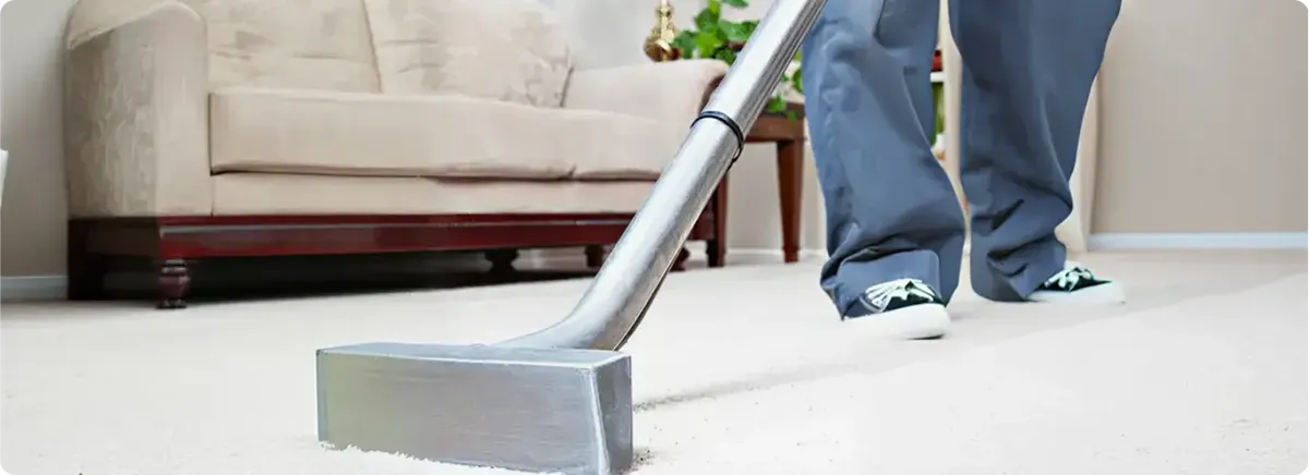 Carpet cleaning technician using a hot-water extraction wand on a light-colored carpet in a living room, Pueblo, CO.