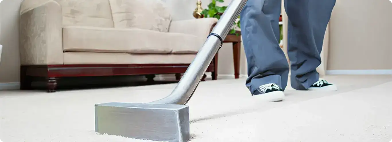 Carpet cleaning technician using a hot-water extraction wand on a light-colored carpet in a living room, Pueblo, CO.