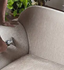 Professional upholstery cleaner deep-cleaning a fabric sofa with a handheld extraction tool and hose Pueblo, CO.