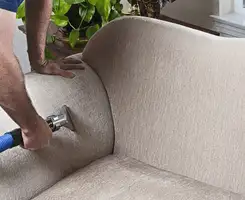 Professional upholstery cleaner deep-cleaning a fabric sofa with a handheld extraction tool and hose in Pueblo, CO.
